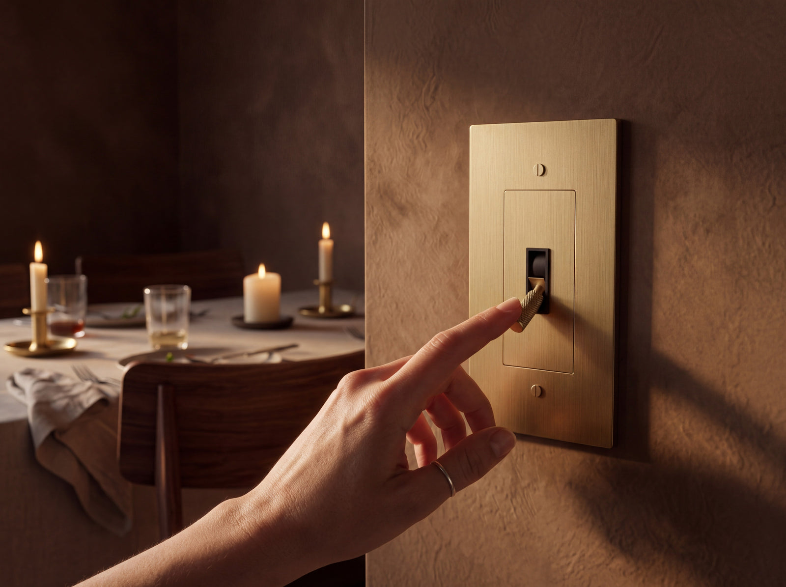 A finger on a brass toggle switch on a plaster wall