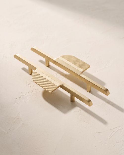 Arco mirrored brass pull pair, packshot on warm ivory plaster